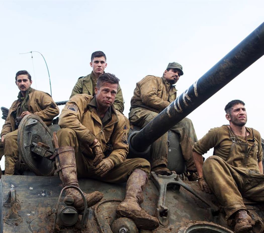 Brad Pitt and costars sit on top of a tank.