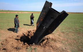 People stand next to an Iranian missile after it fell near Qamishli International Airport, near the Turkish border in the Qamishli district of Hasakah, Syria, on March 4, 2026, amid the U.S.-Israeli conflict with Iran. (Photo by Amjad Kurdo / Middle East Images via AFP)