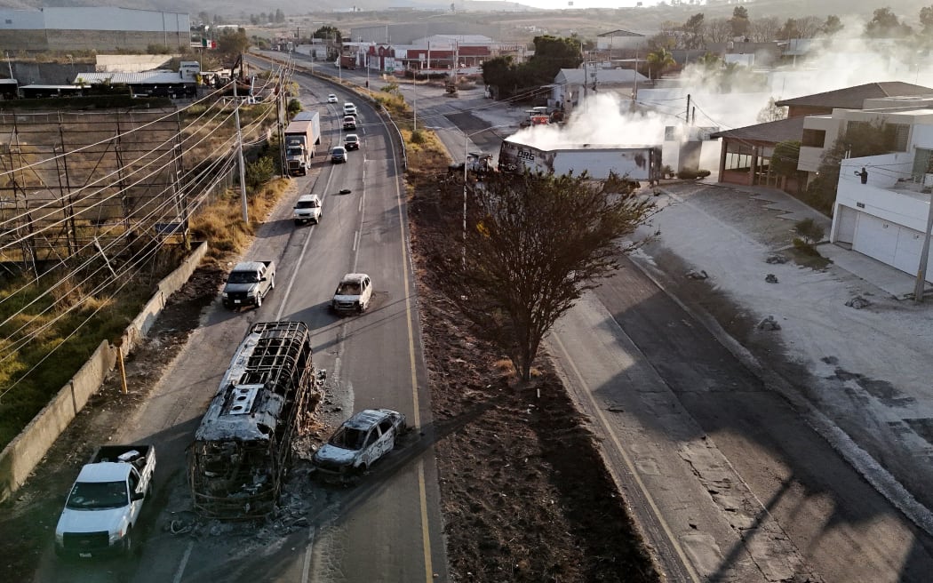 This aerial view shows a burned bus and car, allegedly set on fire by organised crime groups in response to an operation to arrest a high-priority security target, on a highway near Acatlan de Juarez, Jalisco state, Mexico on February 22, 2026. The Mexican army announced that it had killed powerful drug lord Nemesio "El Mencho" Oseguera in an operation that sparked a wave of violence in various parts of the country on February 22, 2026. Gunmen retaliating for the raid blocked more than 20 roads in western Jalisco state, which includes Tapalpa, with burning cars and trucks. The violence spread to other states as well. (Photo by Ulises RUIZ / AFP)