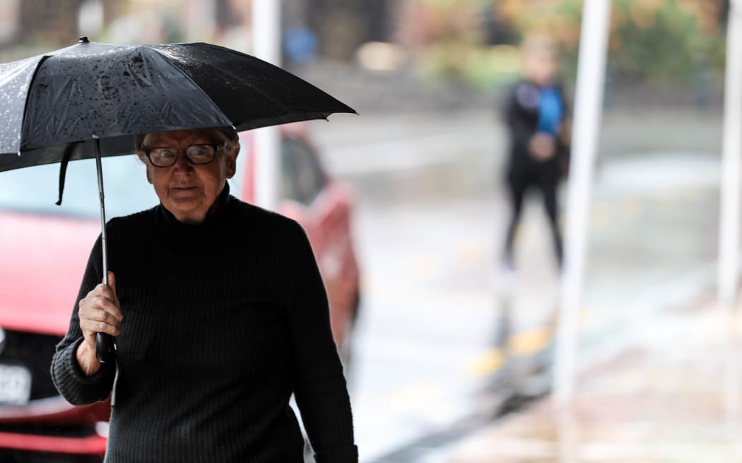 Old woman walks in town centre holding an umbrella.