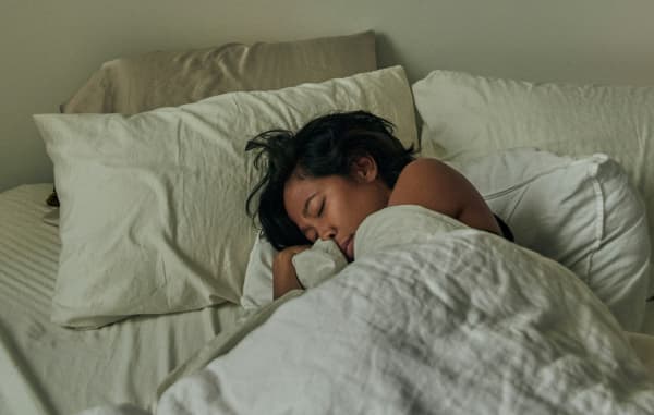 A woman with black hair curls up asleep in bed.