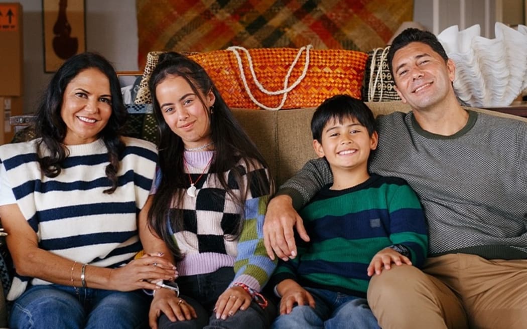 A Maori family of four face the camera with arms around each other.