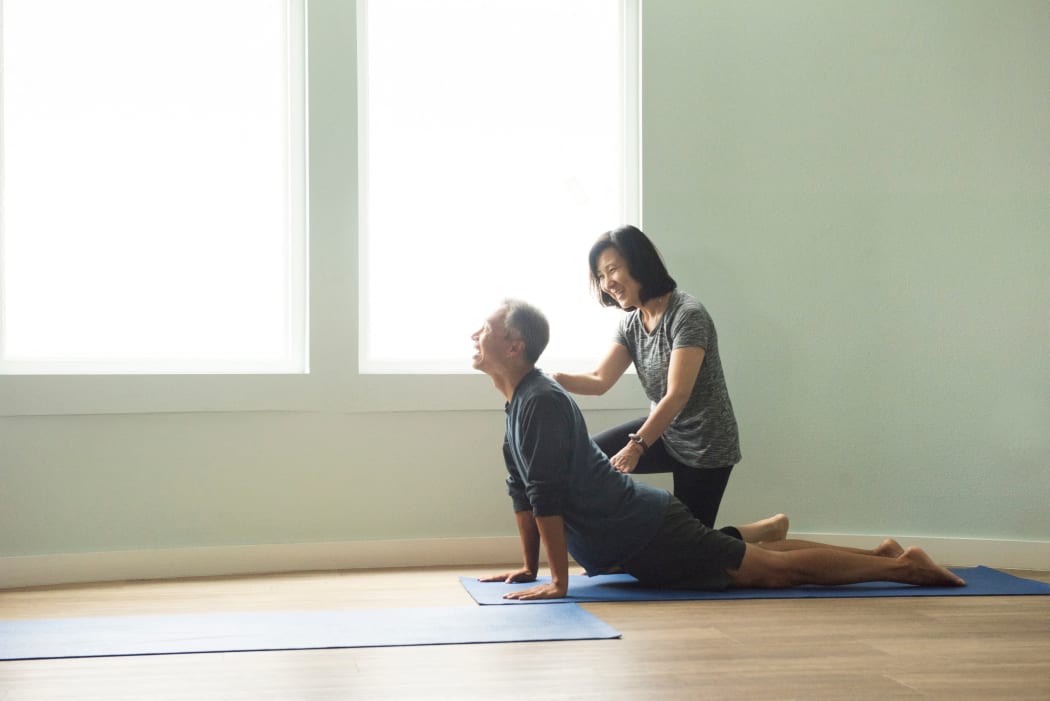 Side view of mature couple doing yoga push up, correcting posture (Photo by David Jakle / Connect Images via AFP)