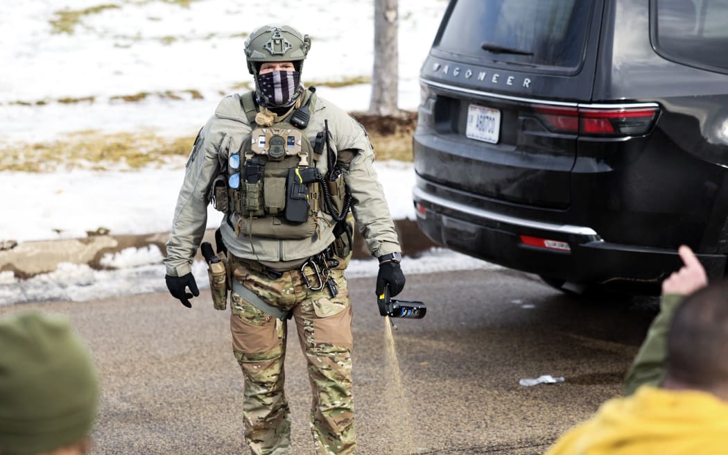 A federal agent monitors the scene as protestors gather near the Bishop Henry Whipple Federal Building in Minneapolis, Minnesota, on January 9, 2026. A US Immigration and Customs Enforcement (ICE) agent shot and killed an American woman on the streets of Minneapolis January 7, leading to huge protests and outrage from local leaders who rejected White House claims she was a domestic terrorist. The woman, identified in local media as 37-year-old Renee Nicole Good, was hit at point blank range as she apparently tried to drive away from agents who were crowding around her car, which they said was blocking their way. (Photo by CHARLY TRIBALLEAU / AFP)
