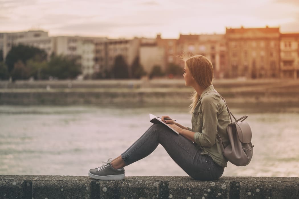 Woman sitting outside looking, observing, writing down in notebook.