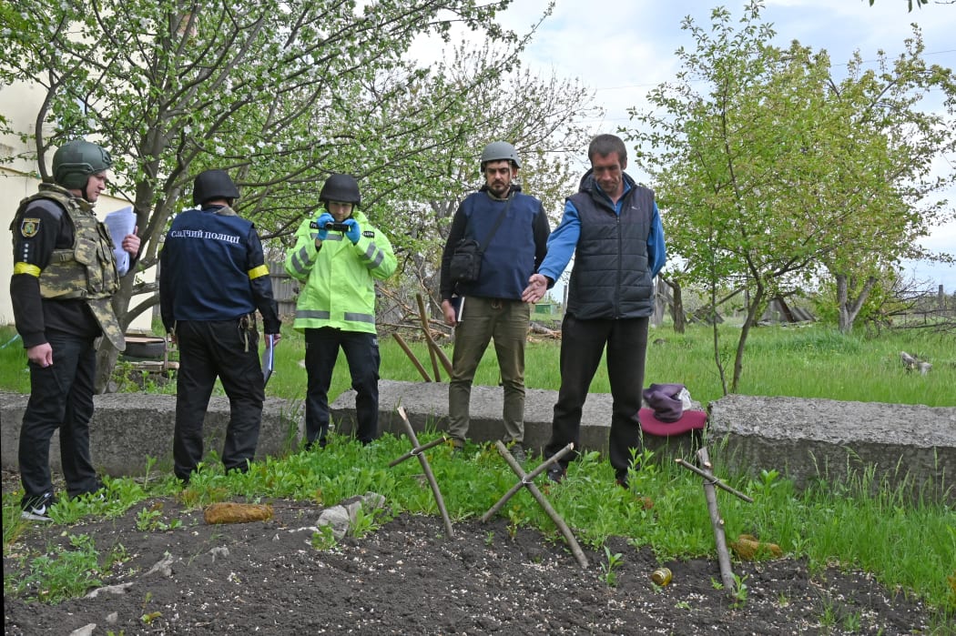 A Ukrainian man shows forensic investigators the grave of three civilians in the yard of a home in the village of Stepanky, near Kharkiv, on Wednesday. Ukrainian officials say they expect to hold many trials of Russian soldiers.