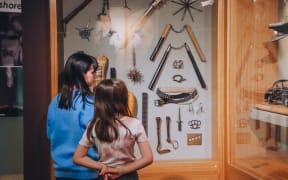 Two children look at glass display cabinets with myriad weapons hanging up.