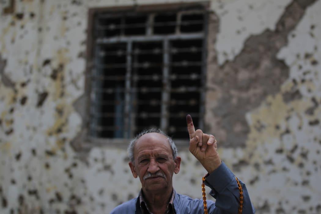 An Iraqi voter shows his ink-stained index finger in front of a damaged wall in western Mosul's Zanjili neighbourhood on May 12, 2018, still partially in ruins from the devastating months-long fight to oust the Islamic State group.