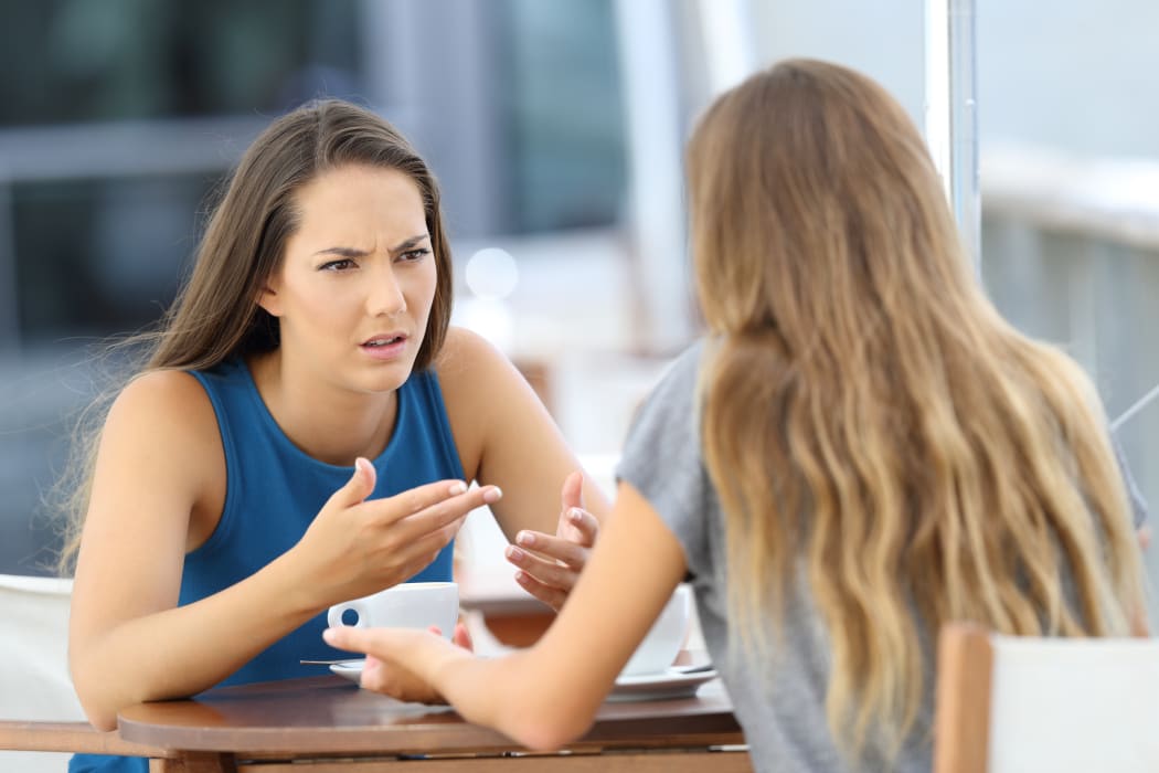 Two angry girls talking seriously sitting in a coffee shop