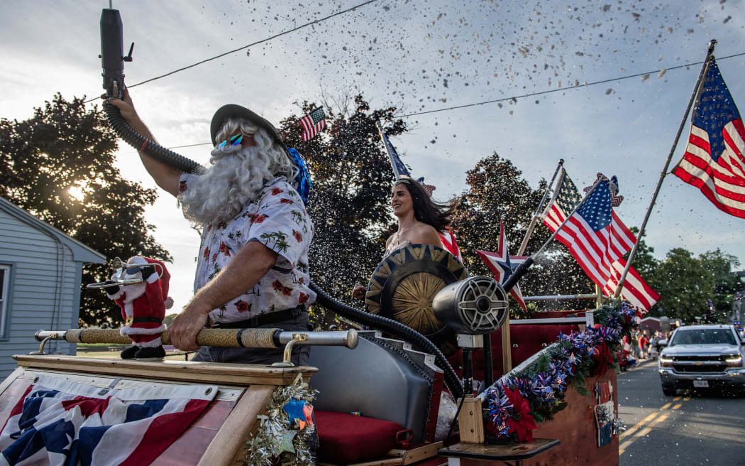 People dressed as Santa Claus and Wonder Woman spray fake snow on attendees as they ride in the Fishtown Horribles Parade, ahead of Independence Day, in Gloucester, Massachusetts on July 3, 2024. The parade is part of the city’s July 4th celebrations. (Photo by Joseph Prezioso / AFP)