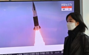 A woman walks past a television screen showing a news broadcast with file footage of a North Korean missile test, at a railway station in Seoul on January 20, 2022,