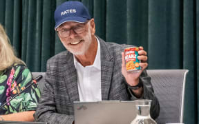 Auckland Mayor Wayne Brown wore a cap with the word 'Rates' on it in a move to mock the governments proposed legislation to cap rates rises. He brought a can of baked beans to the Auckland Council meeting, saying it represents the monthly saving the bill will give to ratepayers.