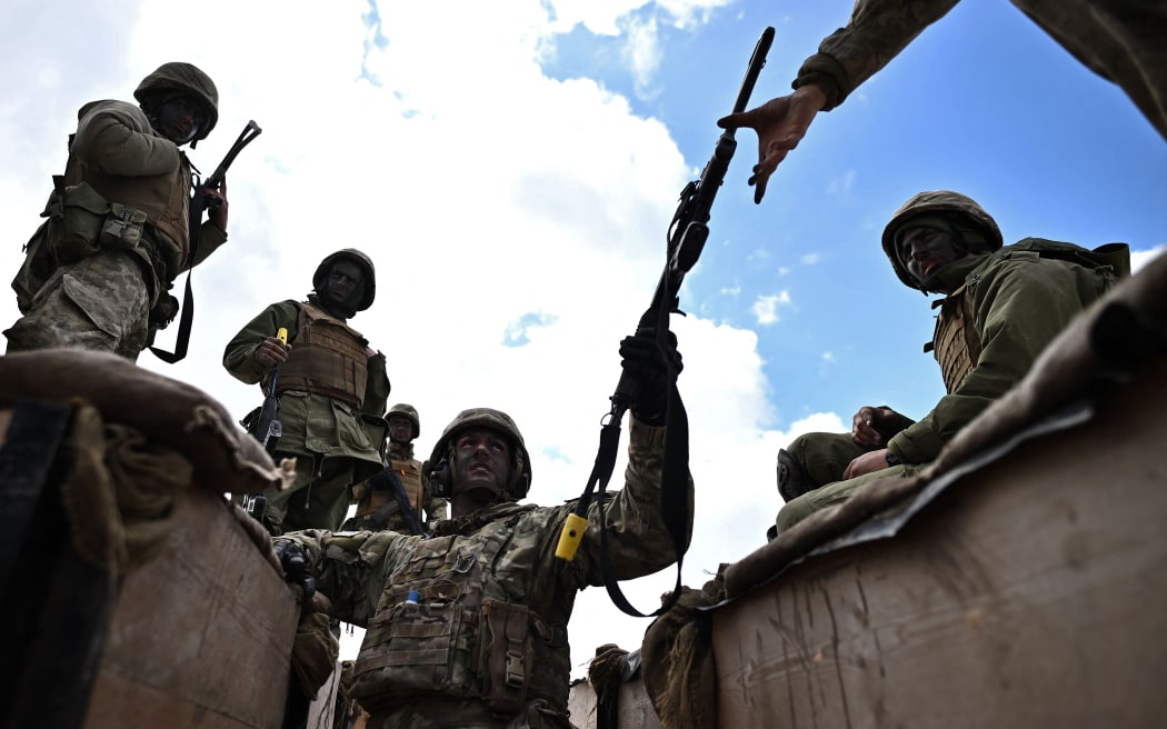 A member of New Zealand's armed forces personnel (C) passes a weapon back to a Ukraine Army recruit after giving a demonstration inside a trench, during a trench warfare training session at a British Ministry of Defence (MOD) training base in southern England on 27 March, 2023.