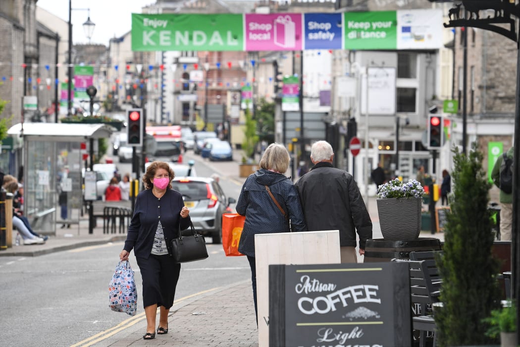 Members of the public, some wearing face coverings due to Covid-19, walk past shops in Kendal in Cumbria, north west England on 21 June 2021.
