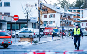 A police officer walks near ambulances at the site of an explosion that ripped through a bar in Crans-Montana on January 1, 2026. Several people were killed and others injured when an explosion ripped through a bar in the luxury Alpine ski resort town of Crans Montana, Swiss police said early on January 1. (Photo by MAXIME SCHMID / AFP)