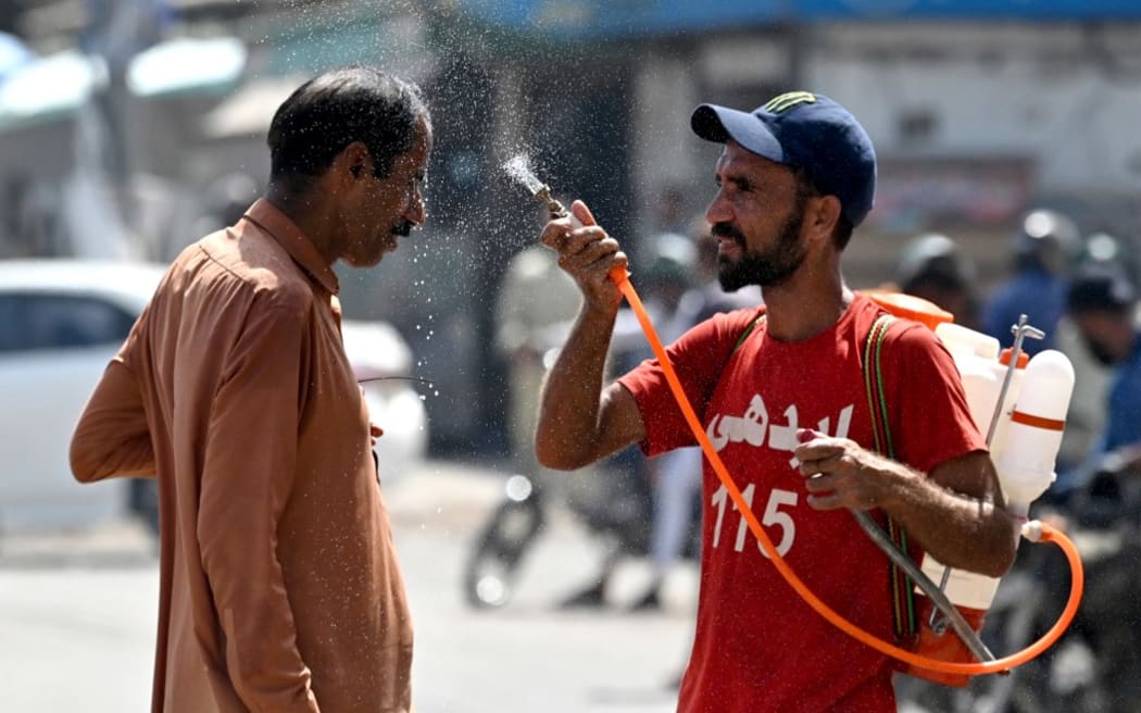 A volunteer sprays water on a bypasser's face along a street during a hot summer day in Karachi on May 30, 2024, amid the ongoing heatwave. (Photo by Asif HASSAN / AFP)