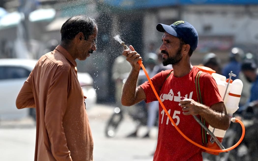 A volunteer sprays water in the face of a passerby on a sweltering summer day in Karachi on May 30, 2024. (Photo: Asif Hassan/AFP)