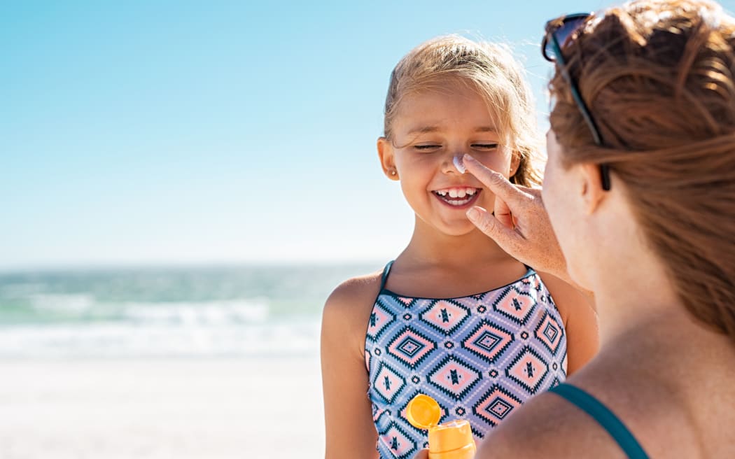 A mother applies protective sunscreen to her daughter's nose at beach.