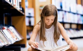 Girl sitting on the floor and reading books in library.