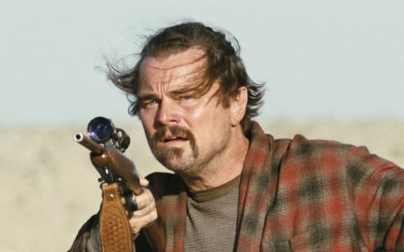 Leonardo DiCaprio holds a gun, his hair is blown around and his face looks wild.