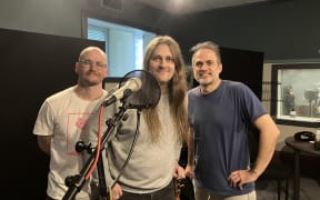 The band Tom Lark stand behind a microphone in the RNZ Wellington studio. They are a three piece band.