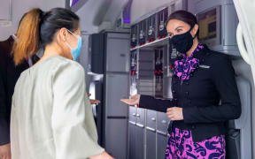A flight attendant welcomes passengers onto an Air New Zealand flight.