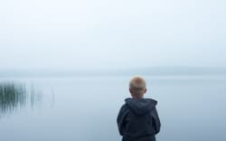 47556115 - sad child sitting alone by lake in a foggy day, back view
