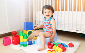 A little boy sitting on the potty by his cot