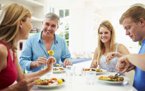 A photo of a family with teenage children eating meal at home together