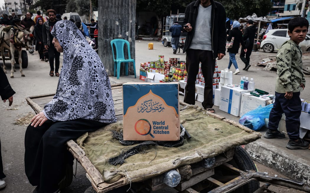 A Palestinian woman sits on a cart next to a box of food rations provided by US  charity World Central Kitchen at a makeshift street market in Rafah in the southern Gaza Strip on March 14, 2024, amid ongoing battles between Israel and the militant group Hamas. (Photo by MOHAMMED ABED / AFP)