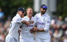 Brydon Carse (c) celebrates the wicket of  Daryl Mitchell with Ben Stokes (L) of England and Shoaib Bashir of England on the first day of the first cricket test between New Zealand and England.