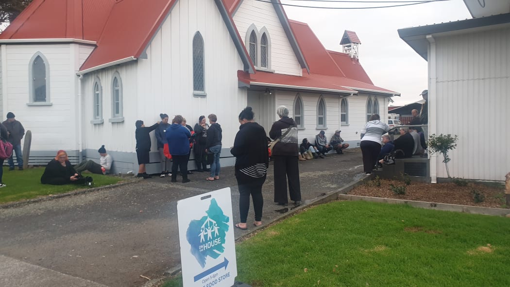 People wait outside the Henui community centre for the On The House pop-up store to open.