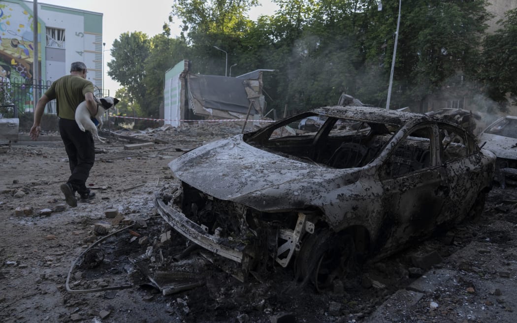 A man carrying a dog walks past the wreckage of cars following mass Russian drones and missile strike on the Ukraine's capital Kyiv on July 4, 2025, amid the Russian invasion of Ukraine. Kyiv said on July 4 that Russia had launched its largest overnight aerial attack on Ukraine over the more than three-year invasion. A representative of Ukraine's air force Yuriy Ignat said the barrage of 550 drones and missiles was a record, adding "this is the largest number that the enemy has used in a single attack." (Photo by OLEKSII FILIPPOV / AFP)