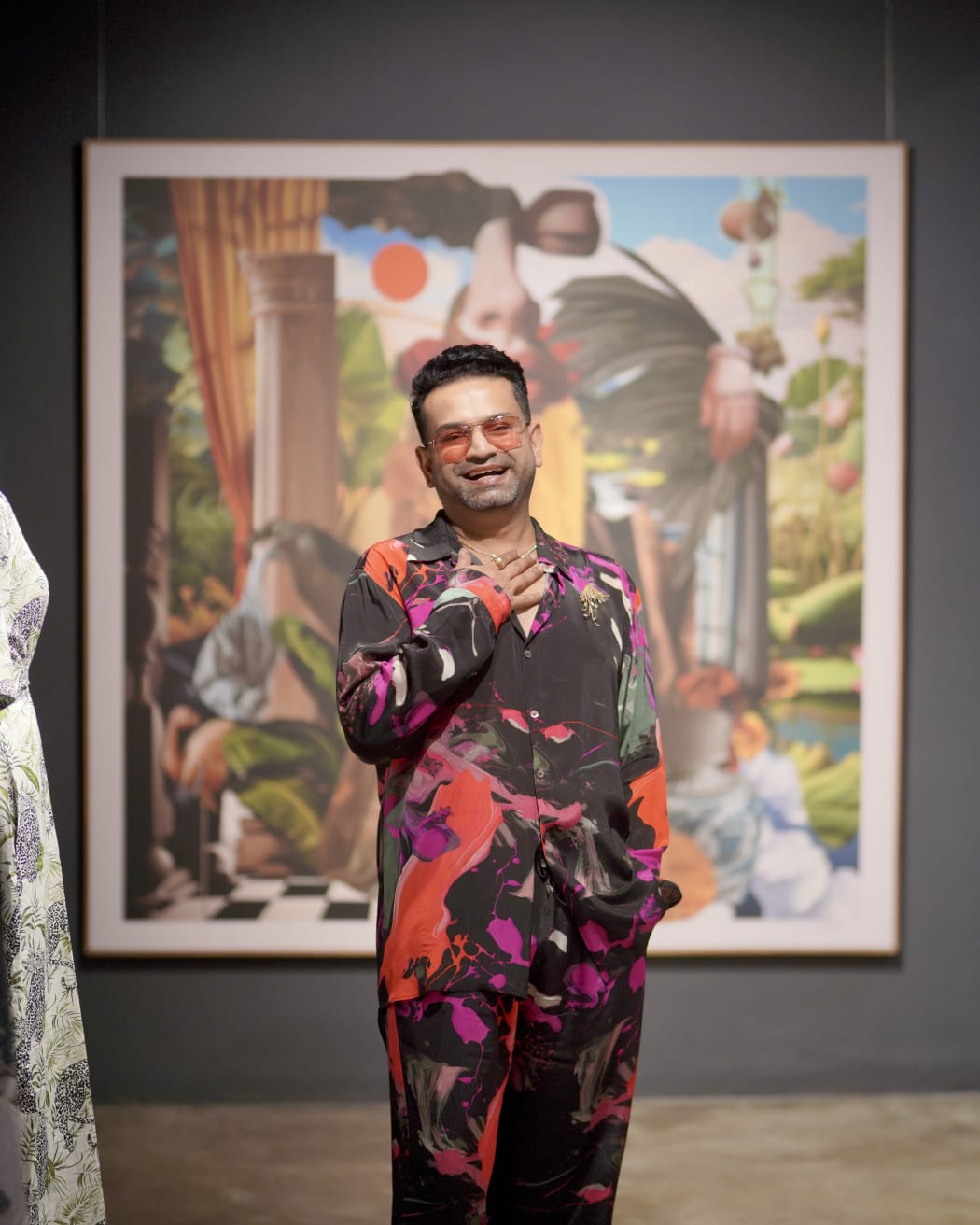 Pranay stands in front of a work of art at a gallery. He wears a shirt with a graphic design across it. He smiles openly.