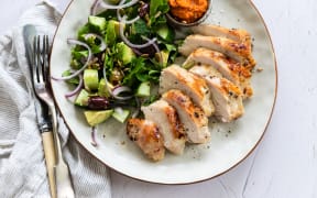 A plate showing some sliced brined and barbequed chicken breasts alongside a salad of lettuce, avocado and red onion.