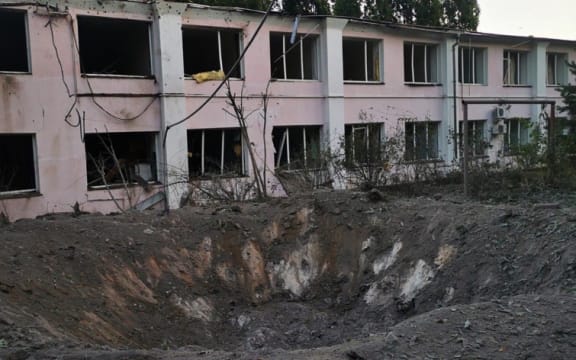 A large hole in the ground in front of a damaged building.