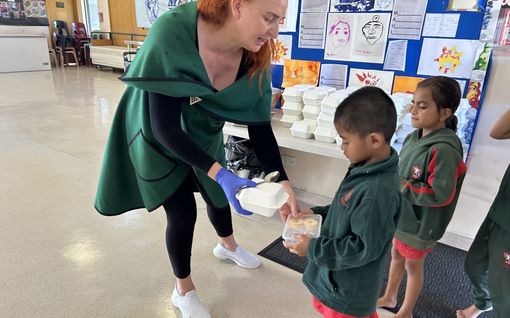 A photo taken at Melville Primary School, depicting an interaction between principal Bronwyn Haitana and a student, where Haitana swaps a box of jam biscuits for a school lunch.