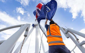 Locky Lockington wrestles with the enormous flag atop the Beehive in order to lower it to half mast for the death of King Tūheitia in August 2024.