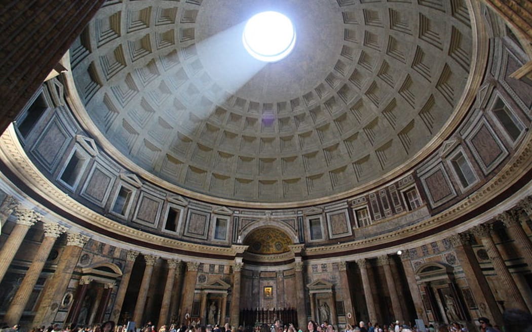 The inside of the Pantheon with light shining down from the Oculus on to tourists standing beneath