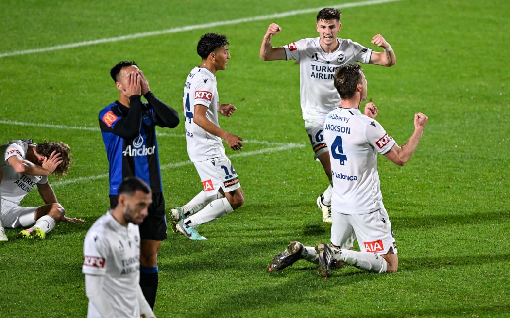 Cam Howieson of Auckland FC holds his face in dejection as Melbourne Victory players celebrate their 2-0 win, A-League semi-final, 2025.