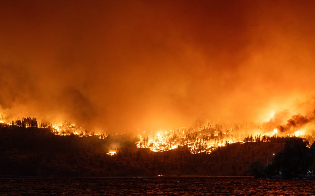 The McDougall Creek wildfire burns in the hills West Kelowna, British Columbia, Canada, on August 17, 2023, as seen from Kelowna. Evacuation orders were put in place for areas near Kelowna, as the fire threatened the city of around 150,000. Canada is experiencing a record-setting wildfire season, with official estimates of over 13.7 million hectares (33.9 million acres) already scorched. Four people have died so far. (Photo by Darren HULL / AFP)