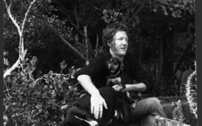 Sam Hunt with a dog and a puppy, sitting on the wreck of a row boat, at an unidentified location. Photograph taken circa 3 December 1975 by an unidentified staff photographer for the Evening Post.