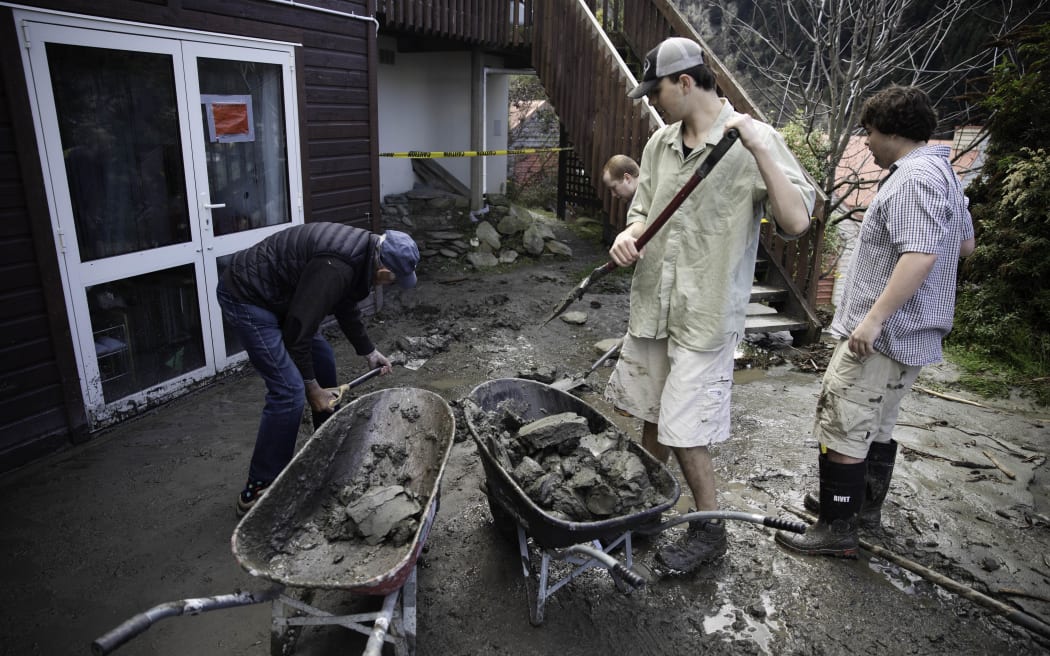 Jasper Thompson, middle right, shovels debris into a wheelbarrow as residents of Reavers Lane, Queenstown begin clearing up after heavy rains.