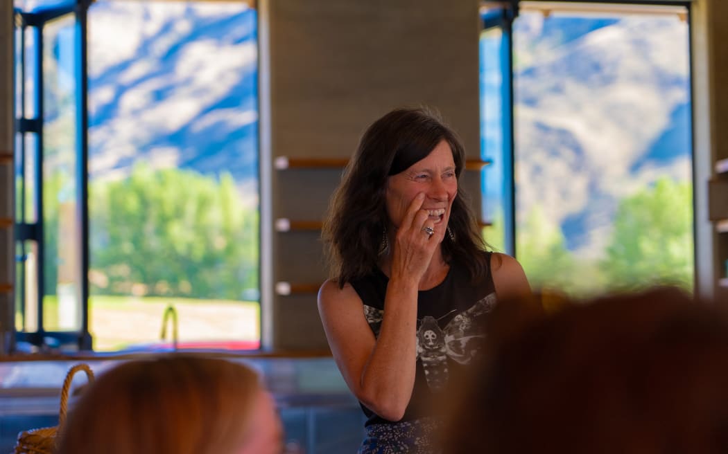 Gina Dempster is stood in front of a few people giving a talk. She is laughing. You can see a mountain behind her.