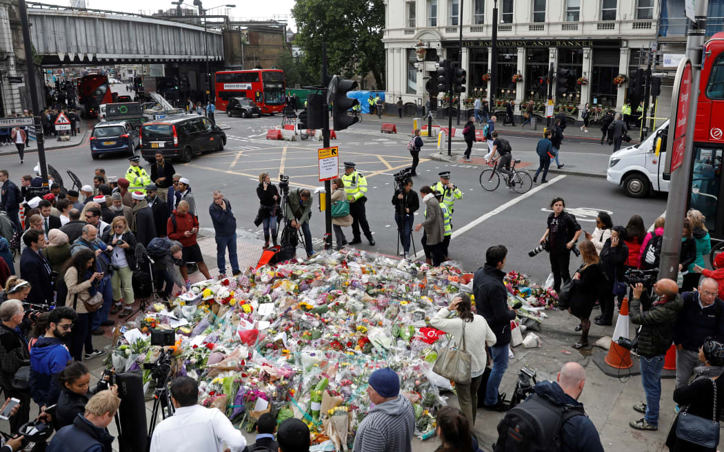 Members of the public and press stand around flowers laid south of London Bridge.