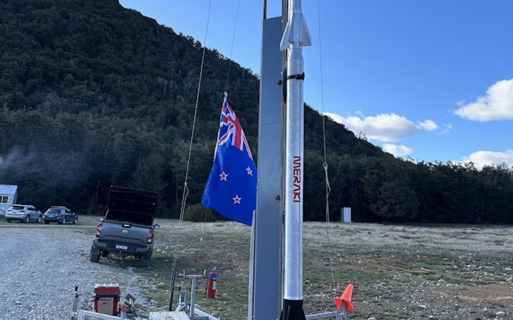 A rocket, in an open field, which is positioned ready for launch on a portable launch pad.
