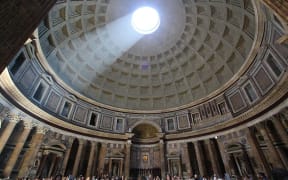 The inside of the Pantheon with light shining down from the Oculus on to tourists standing beneath