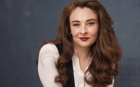 Kaytlin straddles a stool and smiles at the camera.