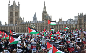 Protesters hold placards and wave Palestinian flags as they walk over Westminster Bridge with the Palace of Westminster, home of the Houses of Parliament behind during a 'March For Palestine' in London on October 28, 2023, to call for a ceasefire in the conflict between Israel and Hamas. Thousands of civilians, both Palestinians and Israelis, have died since October 7, 2023, after Palestinian Hamas militants based in the Gaza Strip entered southern Israel in an unprecedented attack triggering a war declared by Israel on Hamas with retaliatory bombings on Gaza. (Photo by HENRY NICHOLLS / AFP)