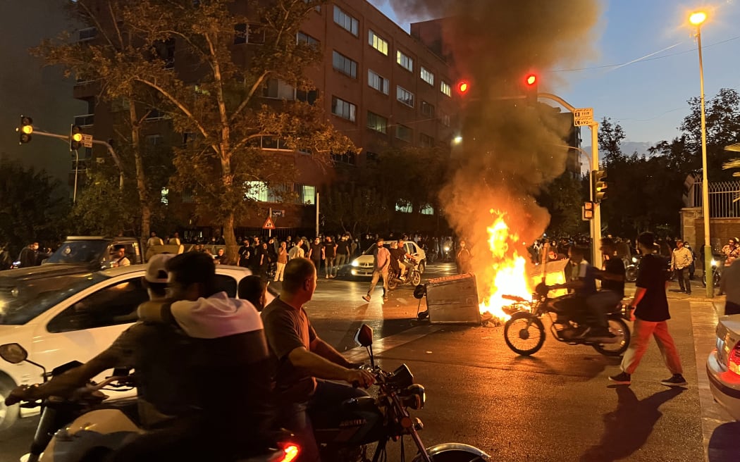 Demonstrators gather around a burning barricade during a protest for Mahsa Amini, a woman who died after being arrested by the Islamic republic's "morality police", in Tehran on September 19, 2022. - Fresh protests broke out on September 19 in Iran over the death of a young woman who had been arrested by the "morality police" that enforces a strict dress code, local media reported. Public anger has grown since authorities on Friday announced the death of Mahsa Amini, 22, in a hospital after three days in a coma, following her arrest by Tehran's morality police during a visit to the capital on September 13. (Photo by AFP)